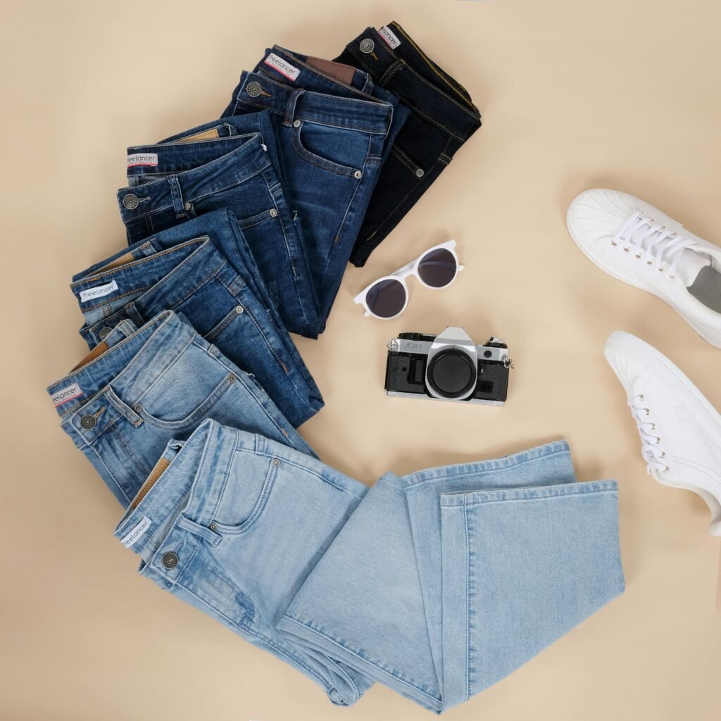 Flat lay showcasing various denim jeans, sneakers, sunglasses, and a camera.